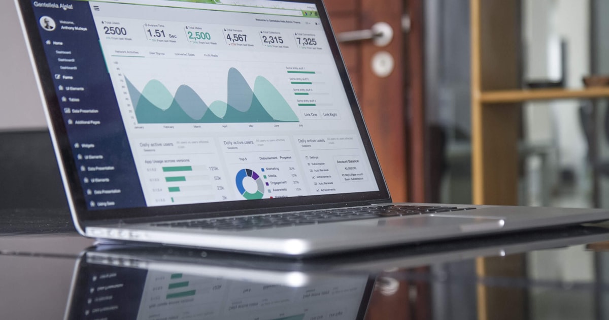 A laptop screen showing a calm analytics dashboard with line and area charts in muted teal and mint green on a dark wooden desk.